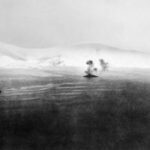 Brytyjski pancernik HMS Warspite (okręt u góry) atakujący baterie lądowe podczas morskiej fazy bitwy o Narwik w kwietniu 1940 roku, nieco ponad miesiąc przed przybyciem estońskiego kontyngentu. Jak widać, teren jest w całości przykryty śniegiem. Zdj. Imperialne Muzeum Wojny / Wikimedia Commons / PD.